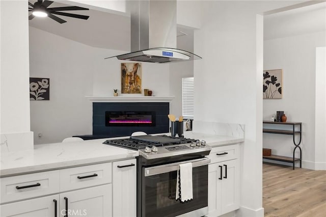 kitchen featuring light stone counters, white cabinets, ventilation hood, stainless steel range with gas cooktop, and a glass covered fireplace