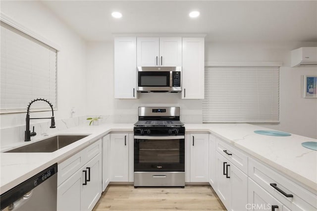 kitchen with light wood-style flooring, appliances with stainless steel finishes, an AC wall unit, white cabinetry, and a sink