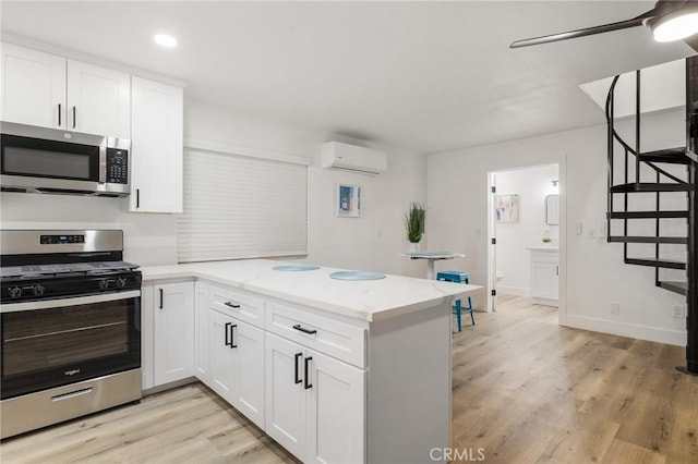 kitchen featuring a wall unit AC, stainless steel appliances, a peninsula, white cabinetry, and light wood finished floors