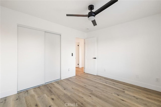 unfurnished bedroom with light wood-style floors, ceiling fan, baseboards, and a closet