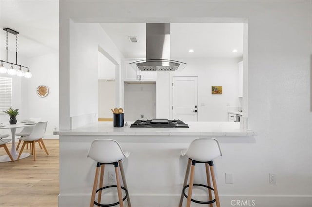 kitchen featuring stainless steel gas cooktop, white cabinets, island range hood, a peninsula, and a kitchen bar