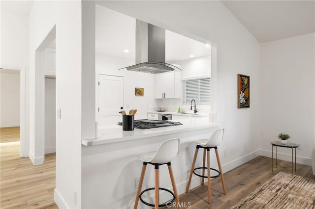 kitchen featuring white cabinets, a breakfast bar area, range hood, light countertops, and light wood-type flooring