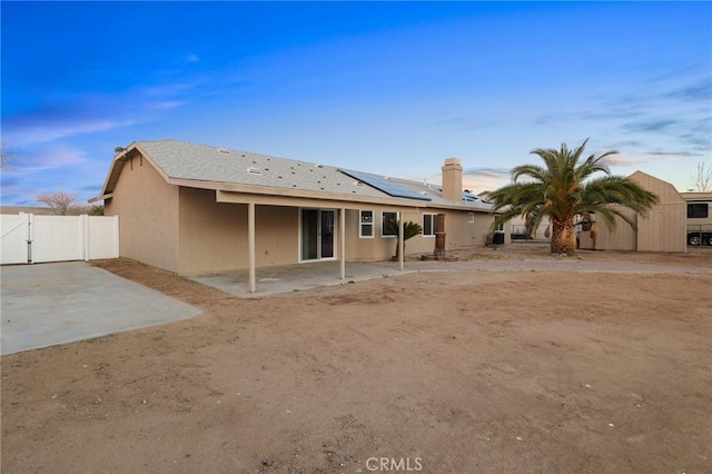 back of house featuring a patio, fence, a gate, roof mounted solar panels, and stucco siding