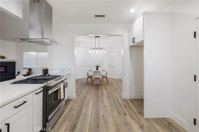 kitchen with light wood-style flooring, visible vents, white cabinets, wall chimney range hood, and stainless steel range with gas cooktop