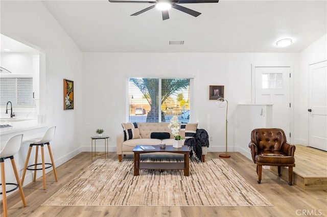 living area featuring baseboards, ceiling fan, visible vents, and light wood-style floors