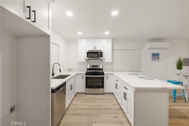 kitchen with light wood finished floors, stainless steel appliances, a sink, a wall mounted air conditioner, and a peninsula