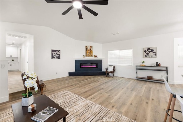 living area with visible vents, a tiled fireplace, ceiling fan, vaulted ceiling, and light wood-style floors