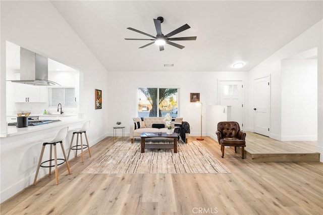 living room featuring baseboards, vaulted ceiling, visible vents, and light wood finished floors