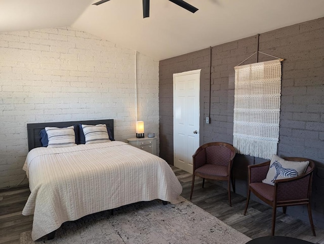 bedroom with vaulted ceiling, dark wood-type flooring, ceiling fan, and brick wall