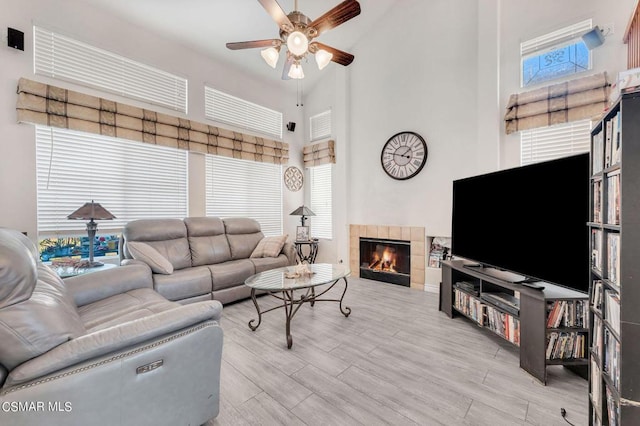 living room with a tile fireplace, a towering ceiling, light hardwood / wood-style flooring, and ceiling fan