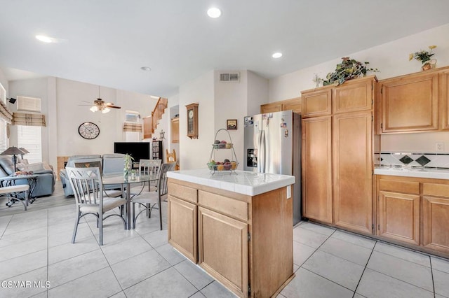 kitchen featuring stainless steel fridge, ceiling fan, light tile patterned floors, tile countertops, and a center island