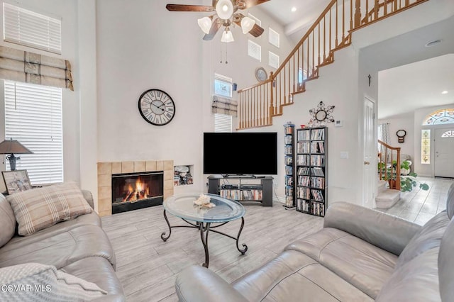 living room with a tiled fireplace, ceiling fan, light hardwood / wood-style floors, and a high ceiling