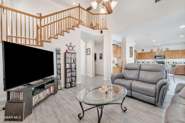 living room featuring a high ceiling, light hardwood / wood-style flooring, and ceiling fan