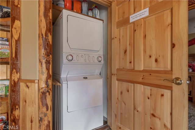 washroom with wood walls and stacked washer / dryer