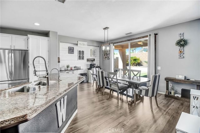 kitchen featuring dark hardwood / wood-style flooring, sink, decorative light fixtures, white cabinetry, and stainless steel refrigerator