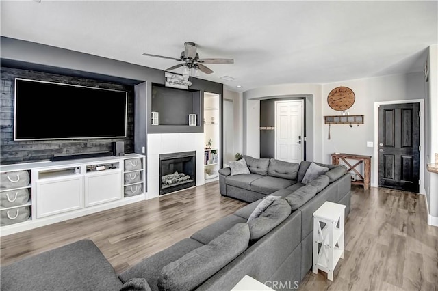 living room with wood-type flooring, ceiling fan, and a tiled fireplace