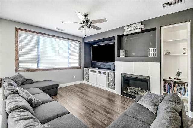 living room with a tile fireplace, wood-type flooring, and ceiling fan