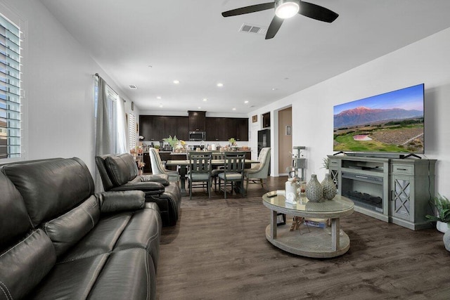 living room featuring a fireplace, ceiling fan, dark wood-type flooring, and plenty of natural light