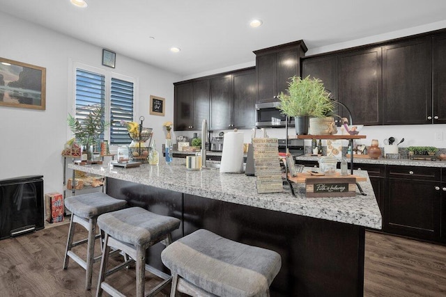 kitchen featuring dark hardwood / wood-style flooring, light stone countertops, a kitchen bar, dark brown cabinets, and a center island