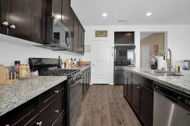 kitchen with appliances with stainless steel finishes, light stone counters, dark brown cabinets, dark hardwood / wood-style floors, and sink