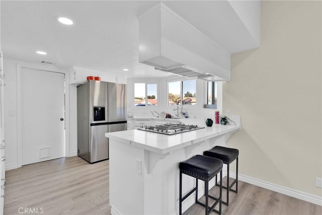 kitchen featuring stainless steel appliances, a kitchen breakfast bar, light hardwood / wood-style flooring, kitchen peninsula, and white cabinets