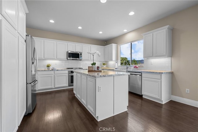 kitchen with a center island, dark wood-type flooring, white cabinets, light stone countertops, and stainless steel appliances