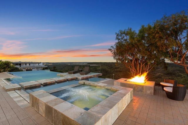 pool at dusk with a patio, an in ground hot tub, and an outdoor fire pit