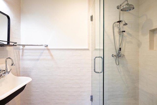 bathroom with a shower with shower door, sink, and tile walls