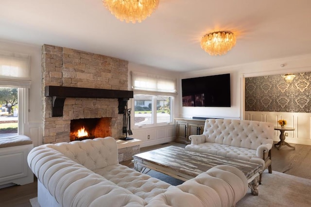 living room with an inviting chandelier, ornamental molding, wood-type flooring, and a stone fireplace