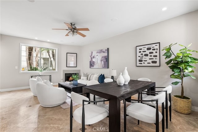 dining room with a warm lit fireplace, recessed lighting, a ceiling fan, and baseboards