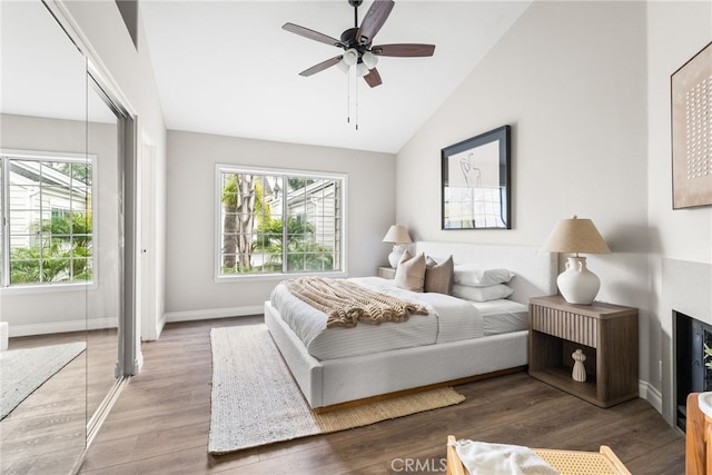 bedroom featuring ceiling fan, a fireplace, wood finished floors, baseboards, and vaulted ceiling