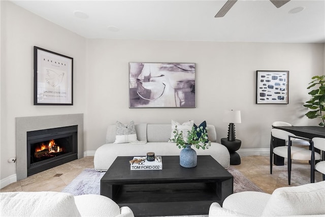 living room featuring a ceiling fan, a lit fireplace, and baseboards