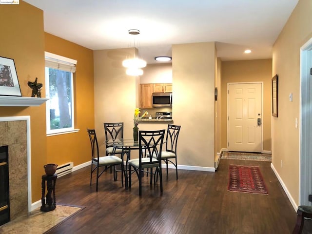 dining space with a fireplace, a baseboard radiator, dark wood-type flooring, and an inviting chandelier