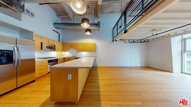 kitchen with stainless steel appliances, a high ceiling, a kitchen island, pendant lighting, and sink