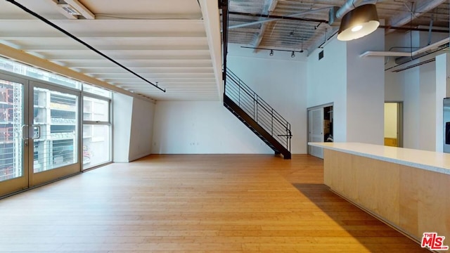 unfurnished living room featuring light hardwood / wood-style flooring, french doors, a high ceiling, and rail lighting