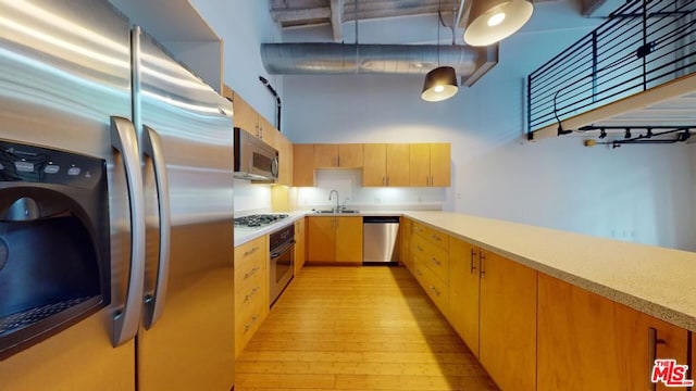 kitchen with sink, hanging light fixtures, appliances with stainless steel finishes, and light wood-type flooring