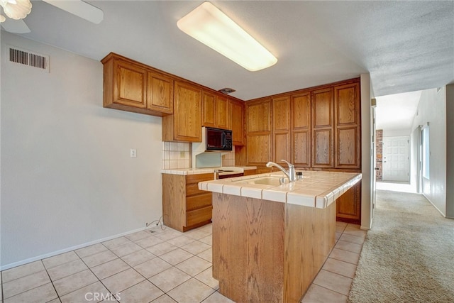 kitchen with light tile patterned flooring, sink, tile counters, and a kitchen island with sink