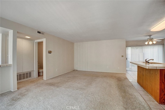 unfurnished living room featuring light carpet, sink, and ceiling fan