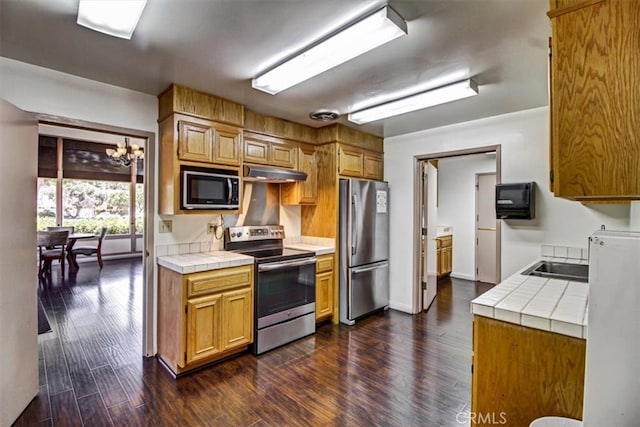 kitchen with tile countertops, dark wood-type flooring, sink, a notable chandelier, and appliances with stainless steel finishes