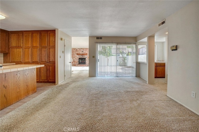 unfurnished living room featuring a textured ceiling, light colored carpet, and a brick fireplace