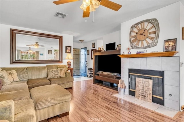 living room with light hardwood / wood-style floors, ceiling fan, and a tiled fireplace