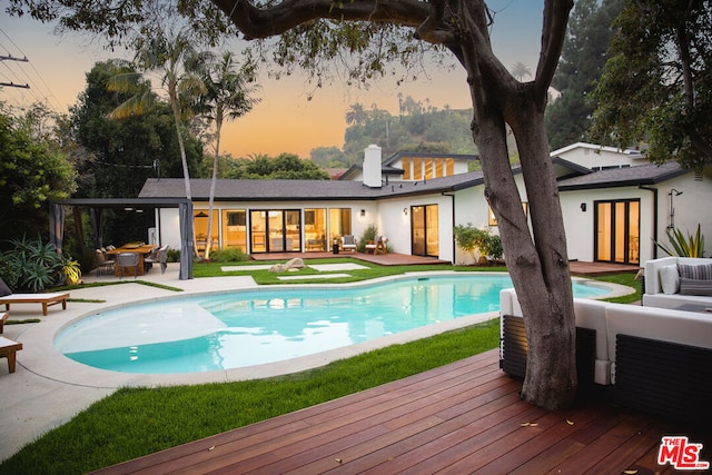 pool at dusk with outdoor lounge area, a patio, and a deck