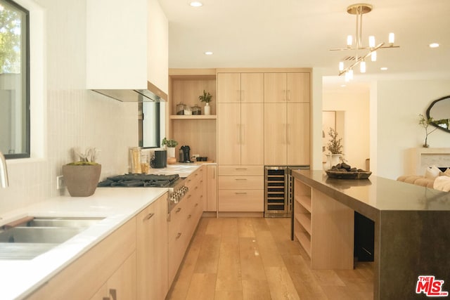 kitchen with sink, wall chimney exhaust hood, hanging light fixtures, light brown cabinets, and light hardwood / wood-style floors