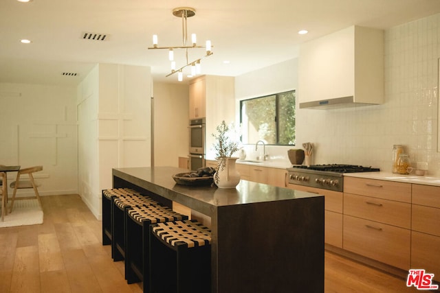 kitchen featuring appliances with stainless steel finishes, light wood-type flooring, wall chimney range hood, pendant lighting, and a kitchen island