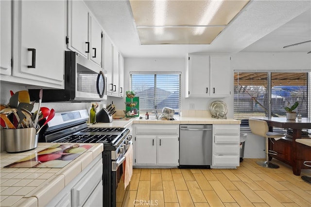 kitchen with sink, light hardwood / wood-style flooring, white cabinetry, stainless steel appliances, and tile countertops