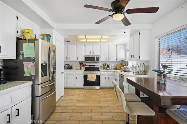 kitchen with stainless steel appliances, white cabinetry, a tray ceiling, and light wood-type flooring