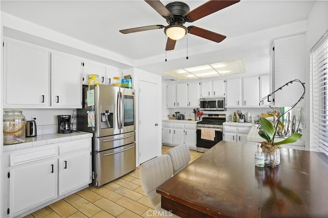 kitchen featuring white cabinets, ceiling fan, appliances with stainless steel finishes, and tile countertops