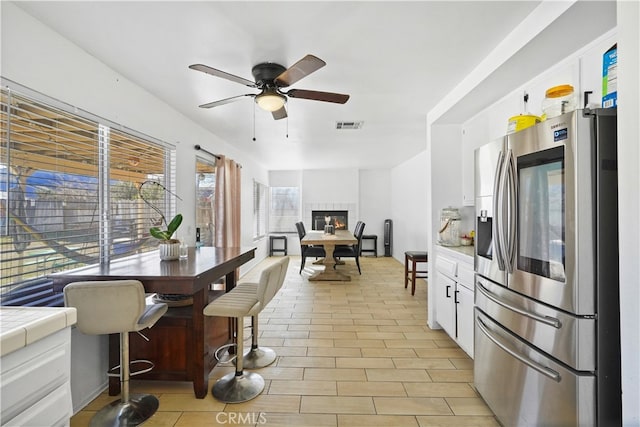 kitchen with ceiling fan, tile counters, stainless steel fridge with ice dispenser, and white cabinetry