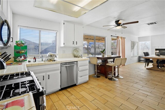 kitchen with white cabinetry, appliances with stainless steel finishes, tile countertops, and light hardwood / wood-style floors