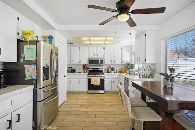 kitchen with a raised ceiling, white cabinetry, light hardwood / wood-style floors, and appliances with stainless steel finishes